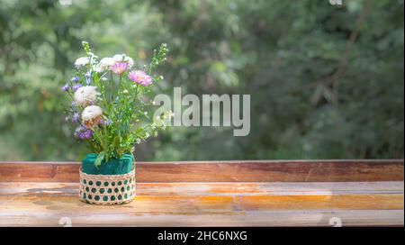 Fiori in un cestino messo su un tavolo di legno con luce solare naturale che si diffonde sottile e spazio copia. Foto Stock