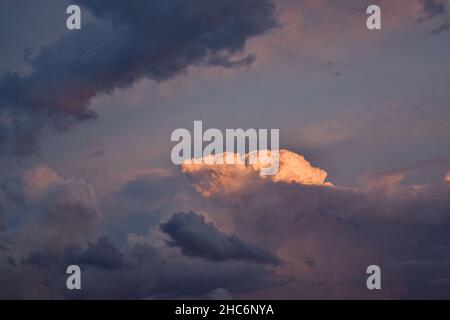 Vista di una grande nuvola in billowing sullo sfondo parzialmente nascosta da lunghe nuvole ombreggiate al tramonto Foto Stock