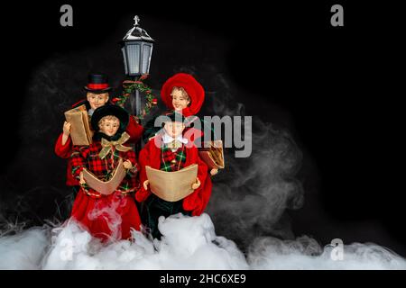 Una famiglia di bambole con costumi tradizionali che cantano una canzone di Natale di notte con un fumo nebbiosa Foto Stock