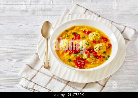 Anar di Ash-e, zuppa invernale di melagrana gialla in due pezzi con polpette, zuppa spessa, in una ciotola bianca su un tavolo di legno bianco testurizzato Foto Stock