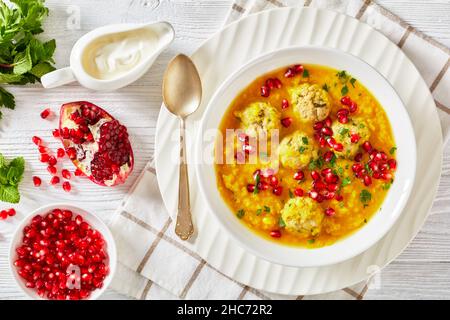 Ash-e Anar, zuppa di melagrana gialla in due pezzi iraniana con polpette di carne, zuppa spessa, in una ciotola bianca su un tavolo di legno bianco testurizzato con ingredienti e Foto Stock