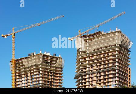 Costruzione di edifici residenziali a più piani di due gemelli utilizzando il moderno metodo della tecnologia monolitica-frame sullo sfondo del cielo blu. Foto Stock