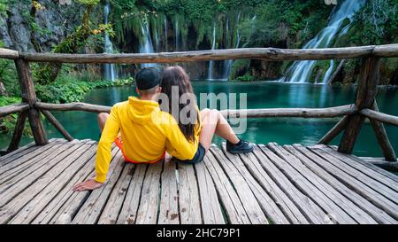 Bella foto di una coppia seduta sul pavimento in legno accanto al parco nazionale dei laghi di Plitvice Foto Stock