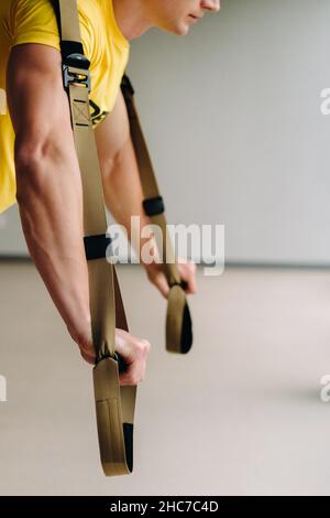 Un atleta maschile focalizzato che svolge un esercizio su loop funzionali in palestra. Foto Stock