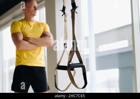 Un atleta maschile focalizzato che svolge un esercizio su loop funzionali in palestra. Foto Stock