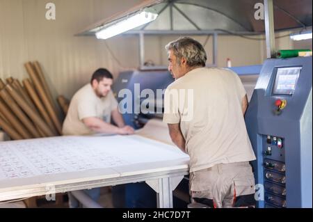 Due operatori tecnici lavorano su una macchina da stampa termica a rullo per sublimazione tessile industriale di alta qualità in digital printshop o Foto Stock