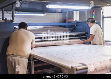 Due operatori tecnici lavorano su una macchina da stampa termica a rullo per sublimazione tessile industriale di alta qualità in digital printshop o Foto Stock