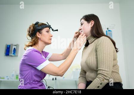 Il medico di ENT femminile esamina i seni del paziente con lo strumento medico nella clinica moderna. Otorhinolaryngologist controlla il naso della ragazza del paziente per Foto Stock