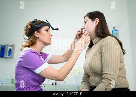 Concetto di otolaringologia. Otorhinolaringologist donna positiva che controlla il naso con otoscopio del suo paziente in ospedale. Congestione nasale, sinusite Foto Stock