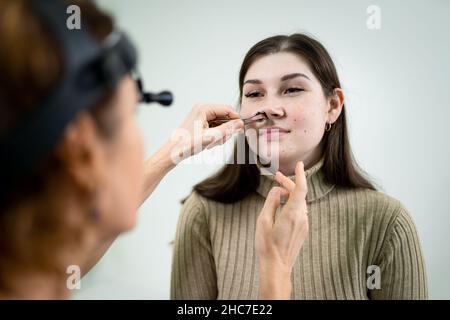 Il medico di ENT femminile esamina i seni del paziente con lo strumento medico nella clinica moderna. Otorhinolaryngologist controlla il naso della ragazza del paziente per Foto Stock