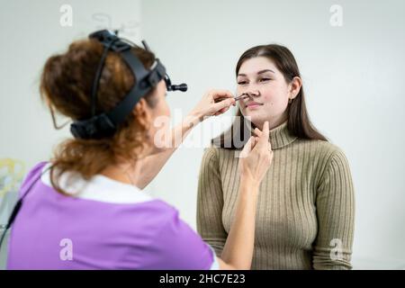Concetto di otolaringologia. Otorhinolaringologist donna positiva che controlla il naso con otoscopio del suo paziente in ospedale. Congestione nasale, sinusite Foto Stock