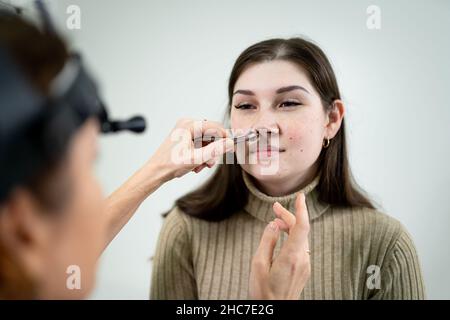 Concetto di otolaringologia. Otorhinolaringologist donna positiva che controlla il naso con otoscopio del suo paziente in ospedale. Congestione nasale, sinusite Foto Stock