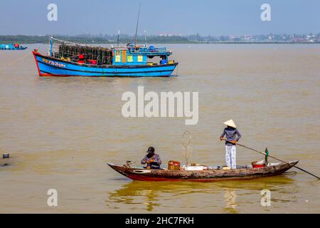 Ragazza con lungo remo spostando la sua piccola barca di fronte un trowler in un Hoi Un villaggio di pescatori area. Foto Stock