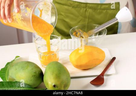 Versare il succo di mango (frullati) con il cubo di mango fresco e la foglia su sfondo bianco, guarnire con foglie di menta. Frutta tropicale preferita Foto Stock