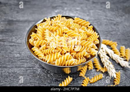 Farina integrale di grano fusilli in una ciotola, spikelets di grano su fondo di legno di tavola Foto Stock