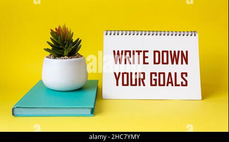 Frase Scrivi i tuoi obiettivi scritti su blocco note e sfondo giallo con diario verde e fiore di cactus. Obiettivi e piani Foto Stock