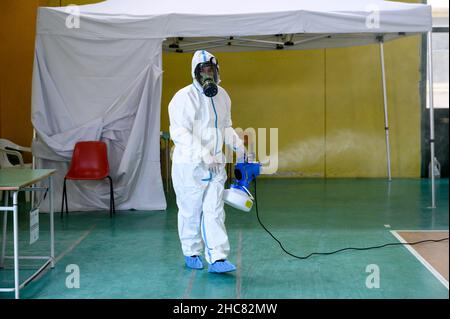 Un operatore sanitario che indossa i dispositivi di protezione individuale (PPE) visto disinfettare la zona, durante la vaccinazione. La campagna anti-Covid19 vaccino nella città turistica di Tropea, sulla Costa degli dei (Costa degli dei) in Calabria (Italia) continua anche a Natale con una giornata aperta nella Sala della palestra comunale. Con l'aumento della paura per la variante Omicron, i giorni di apertura per le festività natalizie e di Capodanno sono stati eliminati dall'Azienda sanitaria Provinciale di Vibo Valentia, con l'aiuto della protezione civile locale (protezione civile). Foto Stock