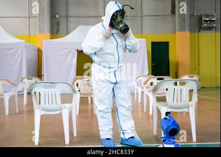 Un operatore sanitario che indossa i dispositivi di protezione individuale (PPE) visto disinfettare la zona, durante la vaccinazione. La campagna anti-Covid19 vaccino nella città turistica di Tropea, sulla Costa degli dei (Costa degli dei) in Calabria (Italia) continua anche a Natale con una giornata aperta nella Sala della palestra comunale. Con l'aumento della paura per la variante Omicron, i giorni di apertura per le festività natalizie e di Capodanno sono stati eliminati dall'Azienda sanitaria Provinciale di Vibo Valentia, con l'aiuto della protezione civile locale (protezione civile). (Foto di Valeria Ferrar Foto Stock