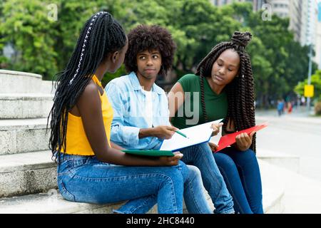 Gli studenti afroamericani maschi e femmine parlano di compiti di università all'aperto in estate in città Foto Stock