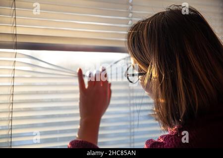 Una donna guarda attraverso i bui alla luce del sole del mattino presto. Foto Stock