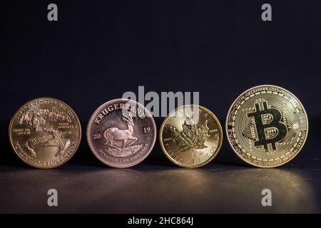 La moneta di bitcoin d'oro si trova accanto ad una moneta di Krugerrand e ad una moneta di oro e di acero canadese Foto Stock