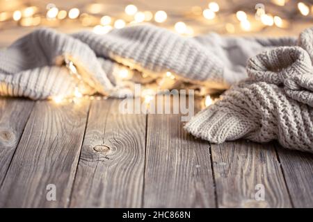 Sfondo accogliente con elementi in maglia e luci bokeh su una superficie di legno. Foto Stock