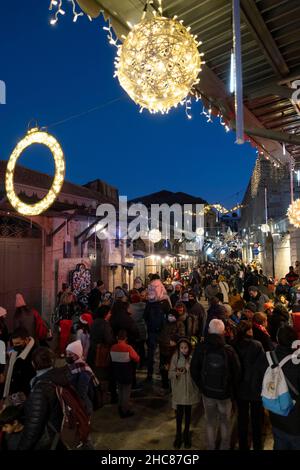 Gerusalemme, Israele. 25th Dic 2021. La gente cammina lungo una strada decorata a Natale Bab el Gadid nel quartiere cristiano della città vecchia il 25 dicembre 2021 a Gerusalemme, Israele. Gli israeliani hanno limitato a viaggiare all'estero, a causa dell'impennata della variante Omicron COVID-19, che riempiva i vicoli a tema natalizio del quartiere cristiano. Credit: Eddie Gerald/Alamy Live News Foto Stock