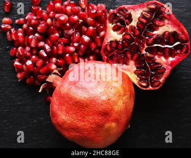 Macro fotografia di due melograni organici uno intero e l'altro tagliato a metà con i suoi semi su sfondo ardesia per illustrazioni alimentari Foto Stock