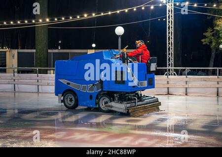 Un operatore dello stadio pulisce una pista di pattinaggio su una moderna macchina per la pulizia del ghiaccio blu. Foto Stock