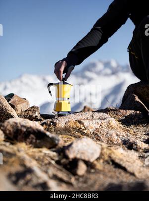 Uomo escursionista che fa il caffè da Yellow Moka mocha pot all'aperto nelle montagne invernali neve. Vecchio stile caffè vintage pot campeggio all'aperto Foto Stock