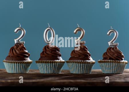 Biglietto di auguri natalizio con tortini di cioccolato e 2022 candele su sfondo blu. Anno nuovo 2022. Foto Stock