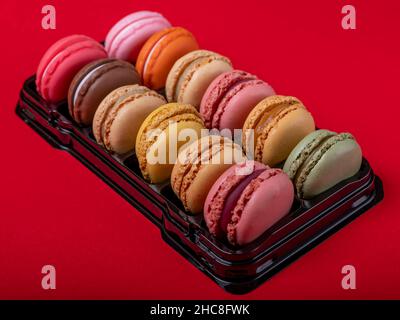 Un vassoio di macaron colorati e gustosi su sfondo rosso Foto Stock