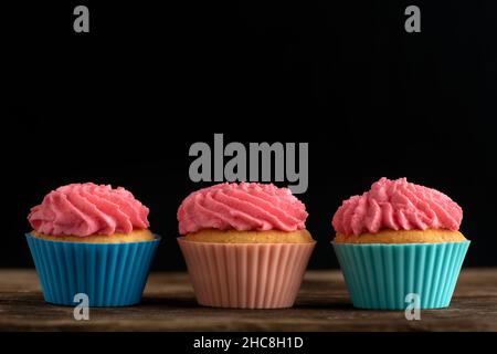 Tre cupcake fatti in casa con glassa di crema di burro rosa su sfondo nero. Spazio di copia Foto Stock