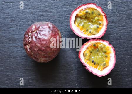 Fotografia di due frutti della passione, uno intero, l'altro tagliato a metà su sfondo ardesia per illustrazioni alimentari Foto Stock