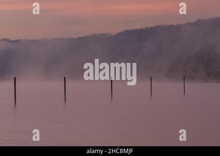 Mattina presto d'inverno durante un'alba vibrante piena di colori e con un velo di nebbia sul lago. I pali da pesca creano piacevoli riflessi Foto Stock