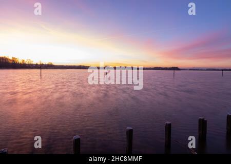 Mattina presto d'inverno durante un'alba vibrante piena di colori e con un velo di nebbia sul lago. I pali da pesca creano piacevoli riflessi Foto Stock