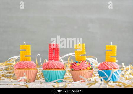 Deliziosi cupcake decorati con candele in forma di numeri 2022 su sfondo grigio. Festa di Capodanno Foto Stock