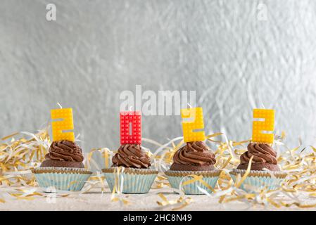 Cupcake festive al cioccolato con crema al burro decorata con 2022 candele numeri. Sfondo in lamina d'argento. Spazio di copia Foto Stock