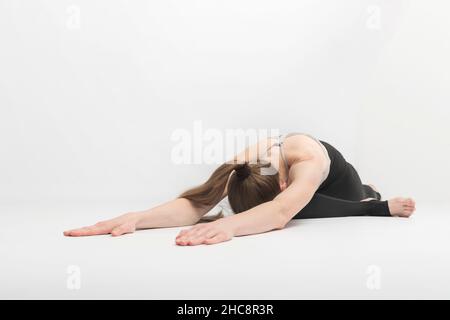 Adho Mukha Kapotasana. Verso il basso Pigeon. Ragazza pratica yoga asanas su sfondo bianco. La giovane donna è impegnata nella ginnastica Foto Stock