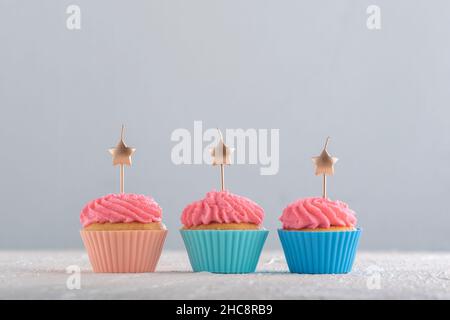 Candele dorate a forma di stella su cupcakes con glassa di crema di burro rosa. Cupcake di compleanno. Cibo per feste Foto Stock