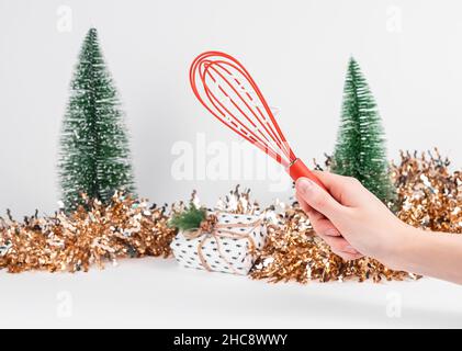 Strumento rosso di whisk a portata di mano e decorazione di Natale e Capodanno sullo sfondo. Foto Stock