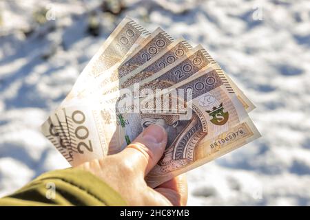 Tenuto in mano denaro polacco, 200 zlotys banconote, sullo sfondo della neve. Il concetto di inflazione e di aumento dei prezzi con il nuovo anno Foto Stock