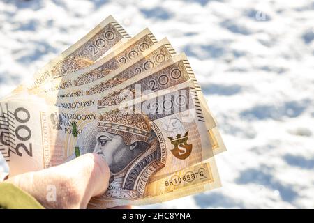 Tenuto in mano denaro polacco, 200 zlotys banconote, sullo sfondo della neve. Il concetto di inflazione e di aumento dei prezzi con il nuovo anno Foto Stock