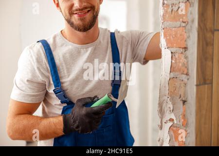 Scatto corto del lavoratore o artigiano usando la spatola e intonacando vecchio muro di cemento con mastice Foto Stock