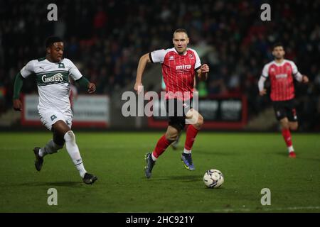 CHELTENHAM, REGNO UNITO. DICEMBRE 26th Niall Ennis di Plymouth Argyle porta la palla in avanti mentre Chris Hussey di Cheltenham Town tenta di rintracciarlo durante la partita della Sky Bet League 1 tra Cheltenham Town e Plymouth Argyle al Jonny-Rocks Stadium di Cheltenham domenica 26th dicembre 2021. (Credit: Kieran Riley | MI News) Credit: MI News & Sport /Alamy Live News Foto Stock