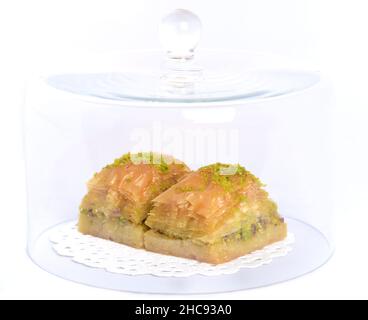 Il baklava fresco, un dolce orientale a base di pasta sfoglia e noci, si trova sotto una cappa di vetro su un dolcetto bianco, di fronte ad uno sfondo bianco Foto Stock