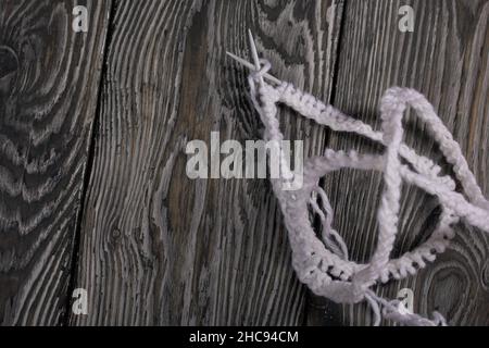 Lavorazione a maglia con aghi. Una matassa di filo bianco e un frammento di prodotto lavorato a maglia. Su assi di pino nero. Primo piano. Foto Stock