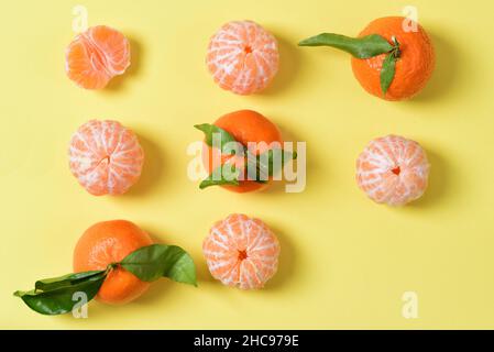 Diversi mandarini si trovano uno accanto all'altro, sbucciati e non sbucciati, un mandarino solo a metà strada. Alcuni frutti hanno foglie verdi. Manca un pezzo Foto Stock