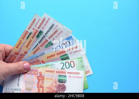 Banconote rubli russe in una mano femminile su sfondo blu. Foto Stock