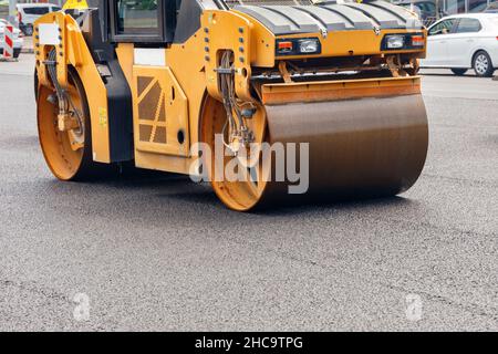 I pesanti cilindri metallici del rullo vibrante giallo della strada compattano l'asfalto fresco sulla strada della città. Spazio di copia. Foto Stock